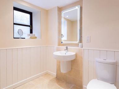 A bathroom with a wall-mounted sink toilet window with towels and a lighted mirror at Thirlmere Cottage in Grasmere
