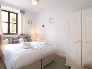 A bedroom with a double bed two plaid pillows and folded towels on it a bedside table with lamp two framed pictures a window with curtains and a white wardrobe at Thirlmere Cottage in Grasmere