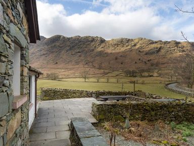 A stone patio and garden wall with a picnic table and hills in the background at Thirlmere Cottage Grasmere
