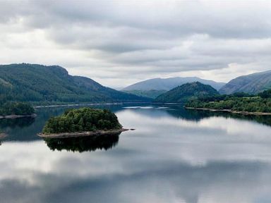 A lake with an island and surrounding hills under a cloudy sky at Thirlmere Cottage in Grasmere
