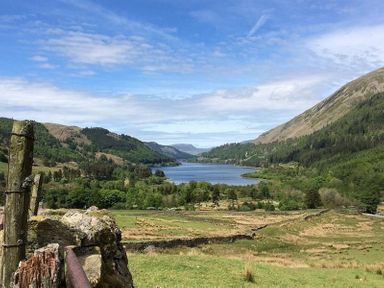 A landscape with a lake surrounded by forested hills and grass fields at Thirlmere Cottage in Grasmere