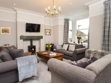 A living room with three sofas a wooden coffee table a wall-mounted television and a wood-burning stove at Thirty Blencathra Street in Keswick