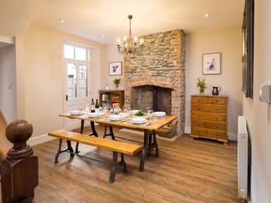 A dining room with a wooden table set for six near a stone fireplace at Thirty Blencathra Street in Keswick