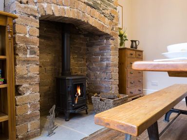 A stone fireplace with a wood burning stove a wooden bench a wooden dresser and a basket of logs at Thirty Blencathra Street in Keswick