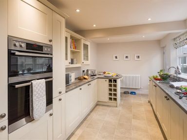 A kitchen with beige cabinets a double oven a countertop with bread and a toaster a wine rack and a window over the sink at Thirty Blencathra Street in Keswick
