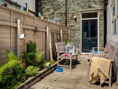 An outdoor patio with wooden benches a stone wall a wooden fence plants and a door at Thirty Blencathra Street in Keswick