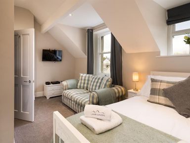 A bedroom with a bed, striped sofa, wall-mounted TV, and a small white cabinet at Thirty Blencathra Street in Keswick