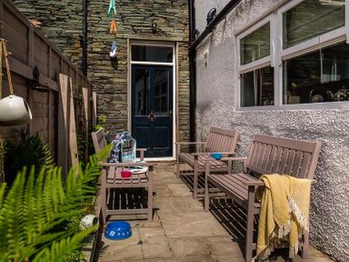 An outdoor patio with two wooden benches, a wooden chair, a stone wall, and a blue door at Thirty Blencathra Street in Keswick