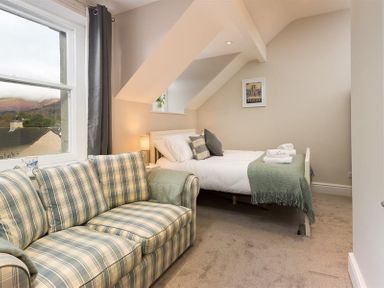 A bedroom with a bed, a plaid sofa, window with a view, and a lamp at Thirty Blencathra Street in Keswick