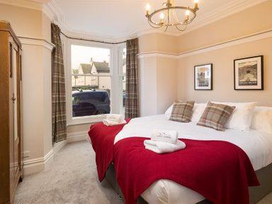 A bedroom with a double bed with red blankets and plaid pillows a wooden wardrobe and a bay window with plaid curtains at Thirty Blencathra Street in Keswick