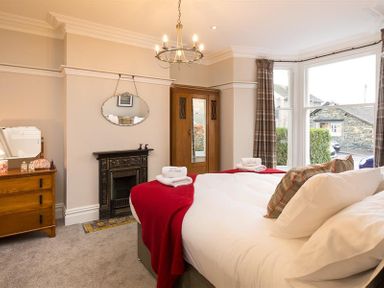 A bedroom with a bed with white sheets and red blanket wooden dresser fireplace and large windows at Thirty Blencathra Street in Keswick