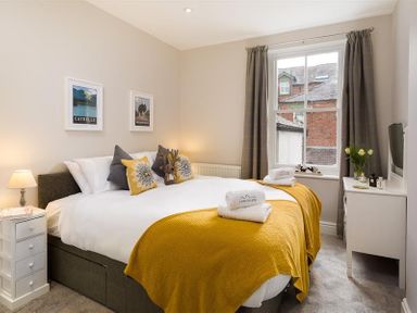 A bedroom with a bed with yellow blankets and pillows bedside table and a window at Thirty Blencathra Street in Keswick