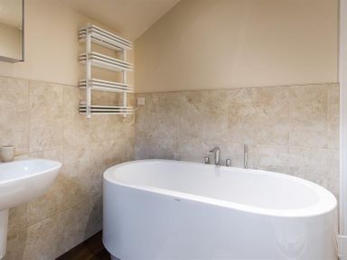 A bathroom with a white freestanding bathtub a sink and a wall-mounted towel radiator at Thirty Blencathra Street in Keswick