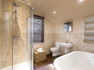A bathroom with a shower, toilet, sink, bathtub, window with blinds, and a wicker basket at Thirty Blencathra Street in Keswick