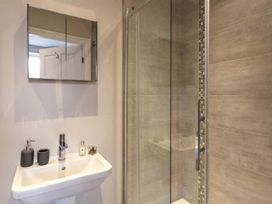 A bathroom with a sink under a mirror cabinet and a glass shower enclosure with tiled walls at Thirty Blencathra Street in Keswick