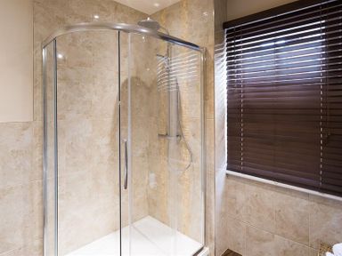 A bathroom with a glass shower enclosure and a window with dark blinds at Thirty Blencathra Street in Keswick
