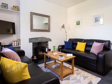A living room with black sofas and colorful pillows around a wooden coffee table with drinks and snacks at Fell Cottage in Ambleside