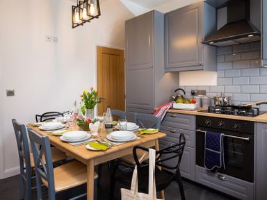 A kitchen with grey cabinets a wooden dining table set with plates glasses and a vase of flowers at Fell Cottage in Ambleside