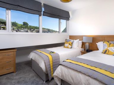 A bedroom with two single beds beside a window with a view of houses and hills at Fell Cottage Ambleside