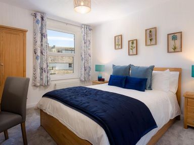 A bedroom with a double bed blue blankets and pillows framed floral pictures on the wall wooden wardrobe and bedside tables at Fell Cottage in Ambleside