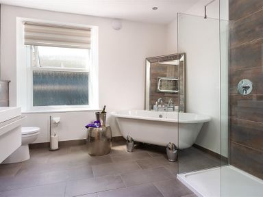 A bathroom with a white bathtub a glass shower enclosure a toilet and a window at Fell Cottage in Ambleside