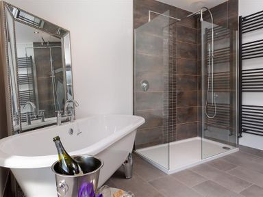 A bathroom with a freestanding bathtub a glass-walled shower and a large mirror at Fell Cottage in Ambleside