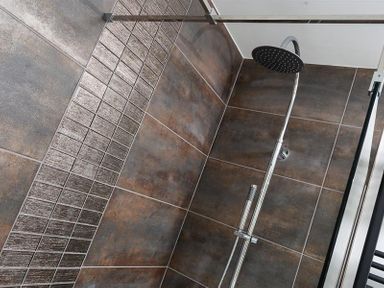 A shower area with brown and textured tiles and a chrome showerhead at Fell Cottage in Ambleside