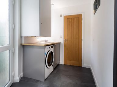 A laundry room with a washing machine a countertop a wooden door and white walls at Fell Cottage Ambleside