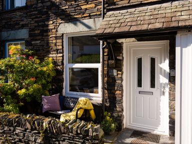 Front entrance of a stone cottage with a white door a bench with cushions and a yellow jacket at Fell Cottage Ambleside