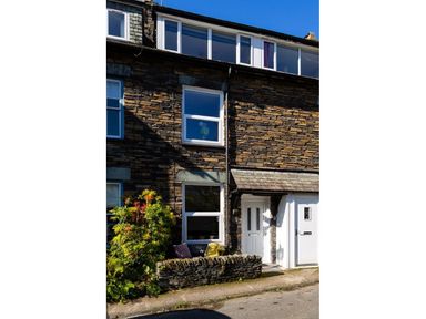 Stone exterior of a house with white framed windows and doors and a small garden area at Fell Cottage in Ambleside