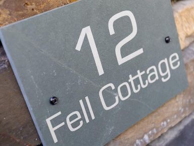 A grey house number sign with the number 12 and name Fell Cottage on a stone wall at Fell Cottage Ambleside