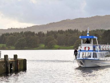 A boat approaching a wooden dock on a lake with trees and hills in the background at Fell Cottage in Ambleside