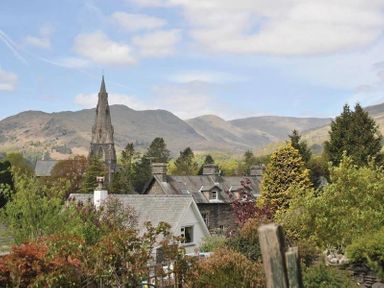 A village with rooftops church tower trees and hills in the background at Fell Cottage in Ambleside