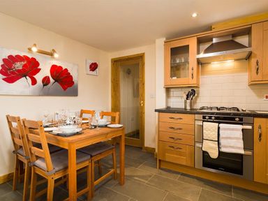 A kitchen with wooden cabinets a stove and a dining table set with dishes and glasses at Agathi in Keswick