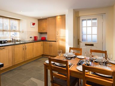 A kitchen with wooden cabinets a dining table set with plates and glasses and a white door in Agathi Keswick