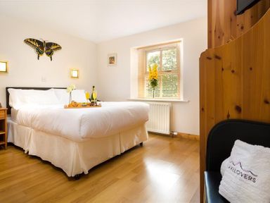 A bedroom with a large bed a tray with drinks on the bed a window with blinds and a chair with a pillow at Agathi in Keswick