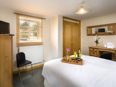 A bedroom with a bed holding a tray with drinks and food a chair a dresser a window with blinds and a wooden closet at Agathi in Keswick