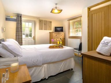 A bedroom with a bed with white linens a wooden dresser a small television and a chair at Agathi in Keswick