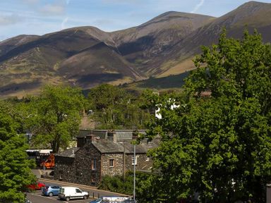 A view of stone buildings with parked cars and trees in front of mountains at Agathi in Keswick
