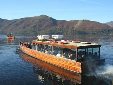 A wooden boat with passengers on a lake with hills in the background at Agathi in Keswick