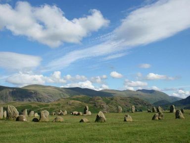 A stone circle on grass with hills and clouds in the background at Agathi in Keswick