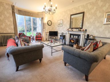 A living room with sofas a glass coffee table armchairs and a fireplace at Stepping Stones House in Ambleside