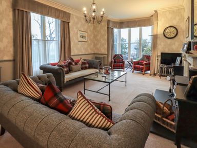A living room with grey sofas red plaid cushions two red plaid armchairs glass coffee table and a chandelier at Stepping Stones House in Ambleside