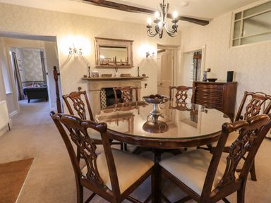 A dining room with a round table and six chairs a chandelier a fireplace and a cabinet at Stepping Stones House in Ambleside