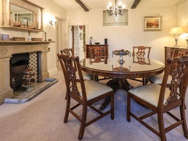 A dining room with a round wooden table and chairs next to a fireplace at Stepping Stones House in Ambleside
