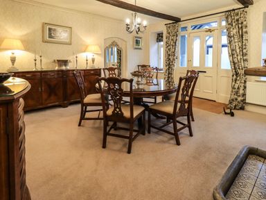 A dining room with a round wooden table and six chairs a sideboard with lamps and candlesticks and double doors with patterned curtains at Stepping Stones House Ambleside