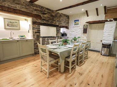 A kitchen with wooden floor a dining table with chairs set for a meal and stone walls at Stepping Stones House Ambleside