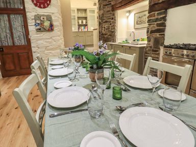 A dining table set with plates glasses cutlery and flowers in a kitchen with stone walls at Stepping Stones House Ambleside
