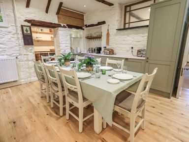 A dining area with a table set for eight with plates and glasses in a kitchen with wooden beams and stone walls at Stepping Stones House in Ambleside