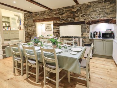 A dining area with a wooden table and chairs set for a meal in a kitchen with stone walls at Stepping Stones House in Ambleside